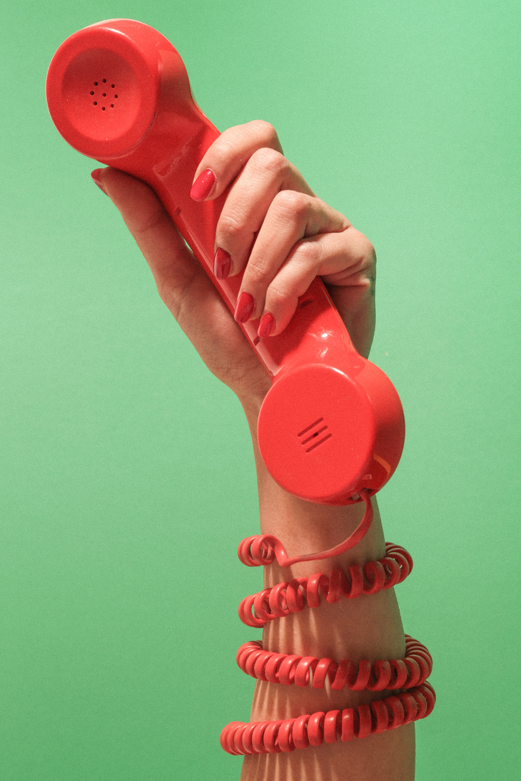 Person's Hand with Red Telephone on Green Background